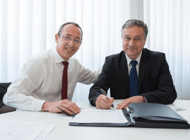 A Man in White Long Sleeves Sitting Near the Man in Black Suit Signing Documents