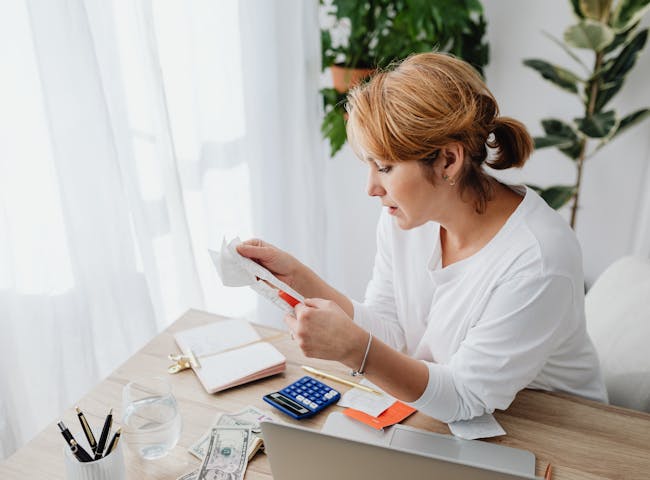 Woman at Wooden Desk Reading a Receipt