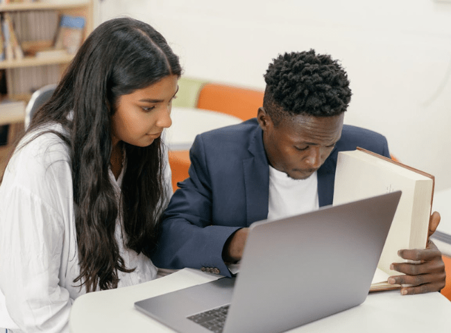 A Teacher and a Student Sitting at Desk Reading a Book