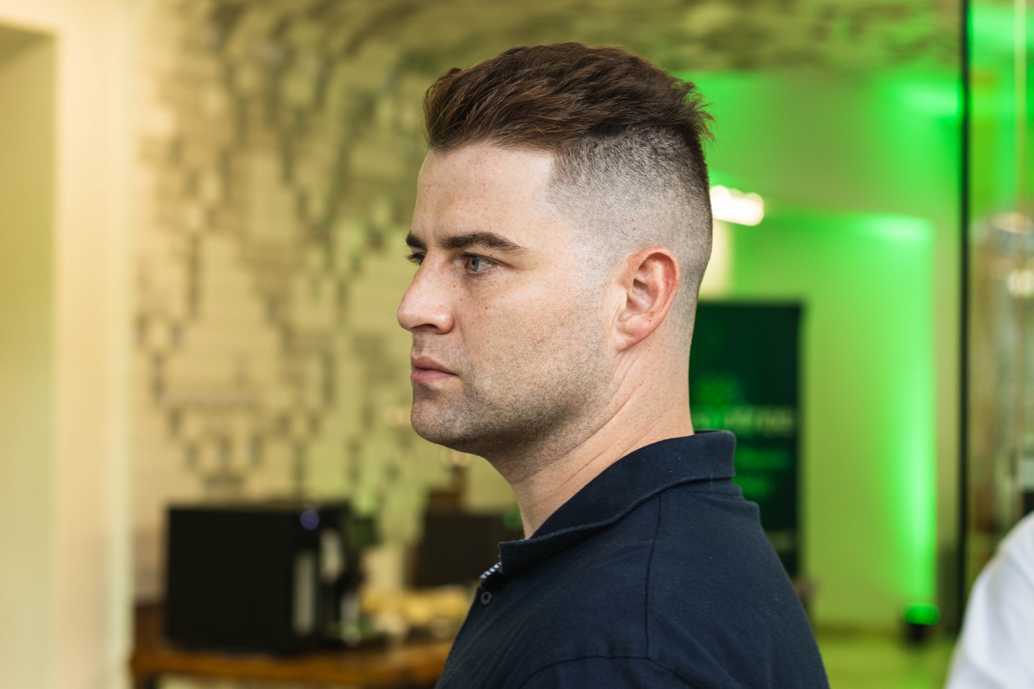 A guest in a dark polo at the evening reception with green accent lighting behind