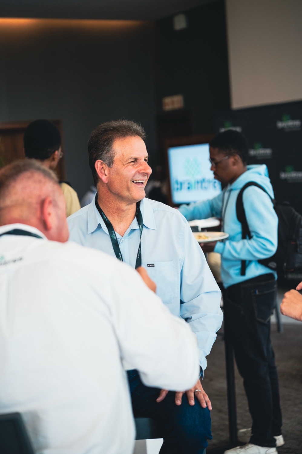 A guest smiling warmly while networking beside the branded backdrop