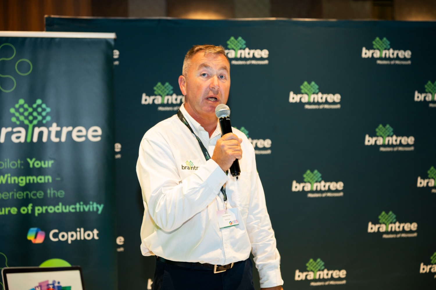 A speaker presenting with a microphone beside the branded Braintree and Copilot banner