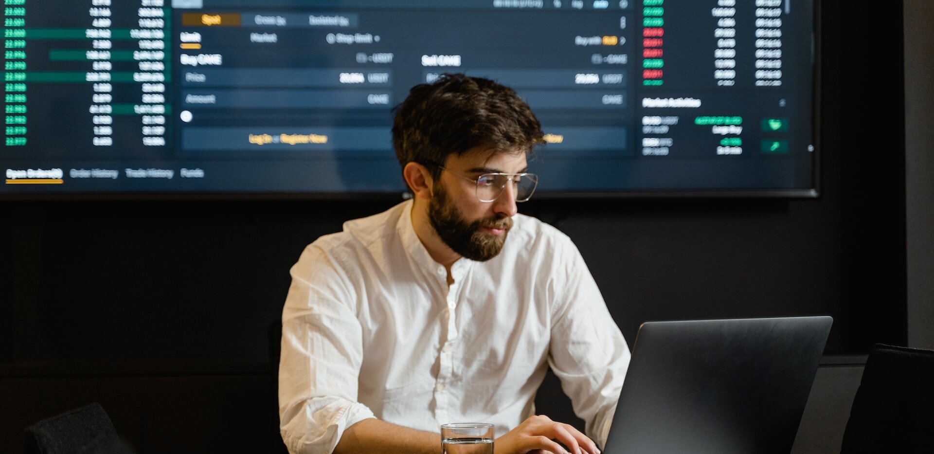 man working with a laptop and a screen of data behind him